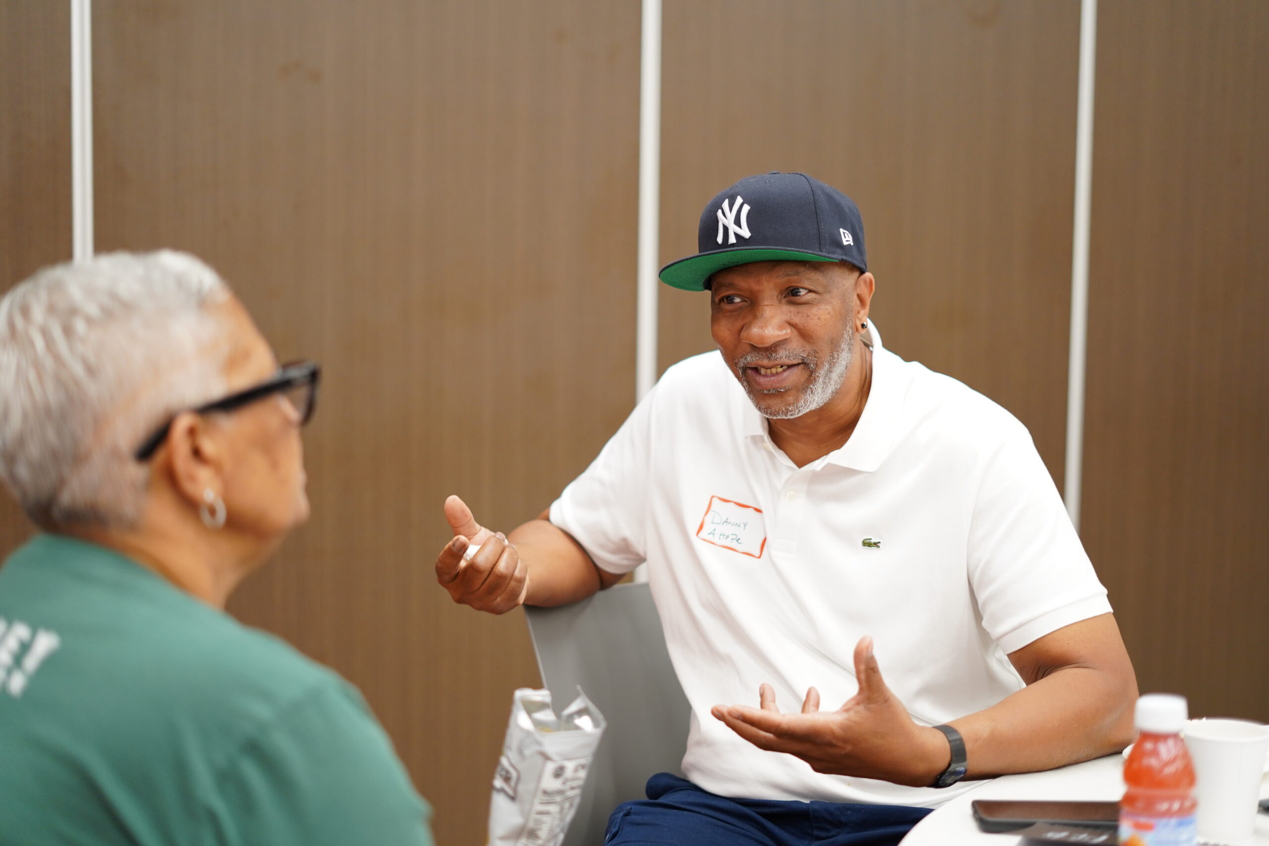 Man in a baseball cap and white polo talking with another participant at a MAHRWC training