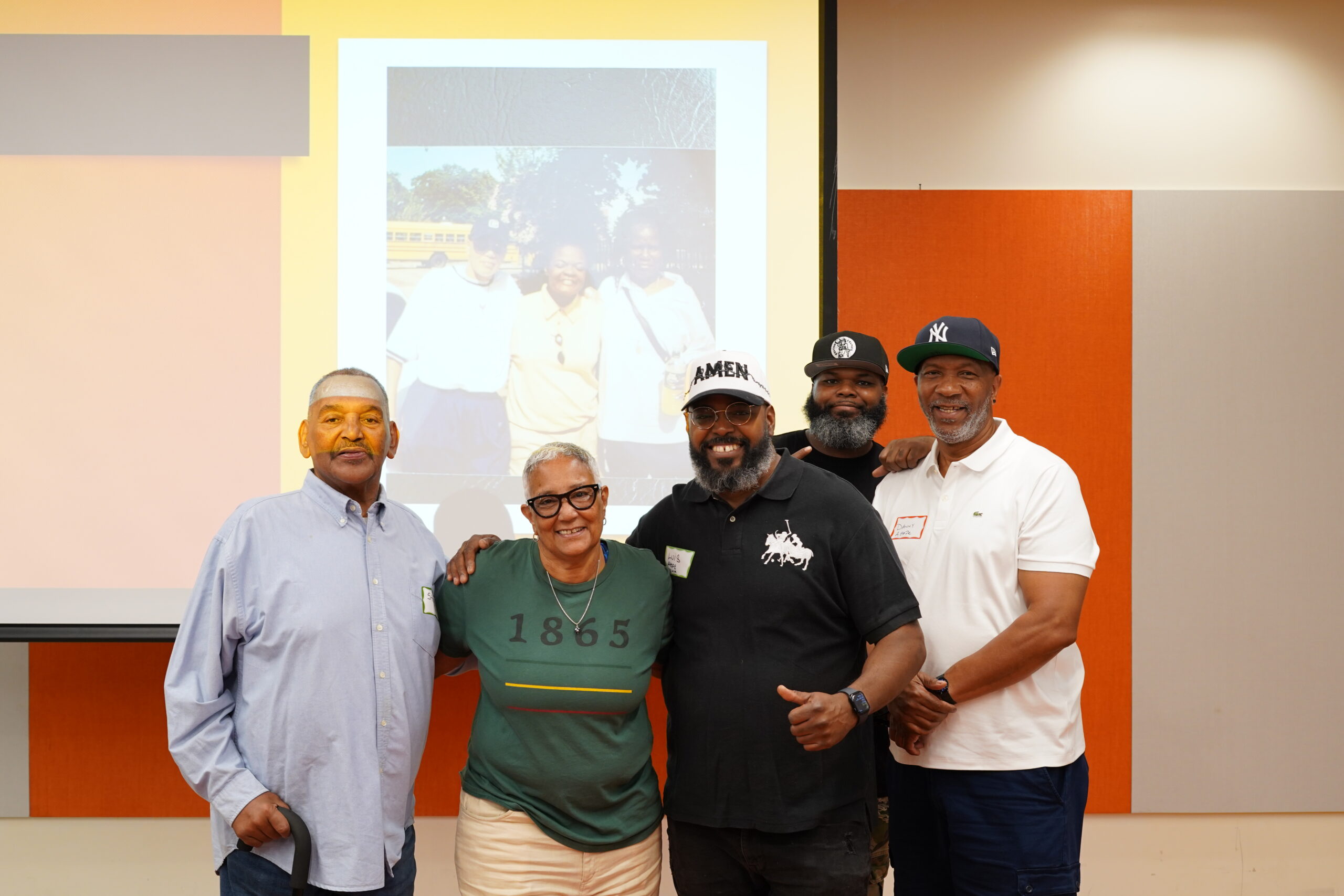 Five MAHRWC training participants posing arm in arm in front of a projected photo